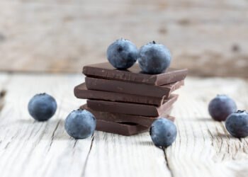 Dark chocolate stack and fresh organic blueberries on wooden table. Natural light, selective focus.