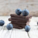Dark chocolate stack and fresh organic blueberries on wooden table. Natural light, selective focus.